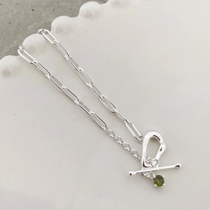 Detail of silver toggle clasp bracelet with paperclip chain and green gemstone charm