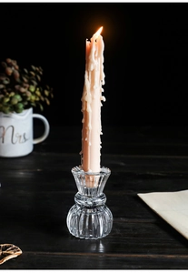Detailed close-up of a wavy glass candle holder with a lit pink taper candle