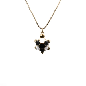 Close-up of golden turtle pendant with a black and white soccer pattern shell on white background