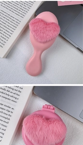 Foldable heart-shaped plush hairbrush with mirror shown in a cozy desk setting