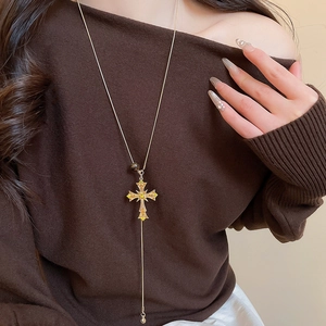 Detail of a gold cross pendant necklace with yellow crystals on a brown sweater