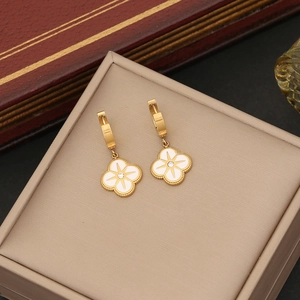 Close-up of gold clover earrings with white enamel and centered crystal inlay detail
