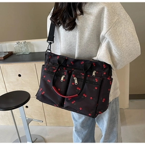 Close-up of black tote bag with red cherry prints shown on a model in a minimalist room