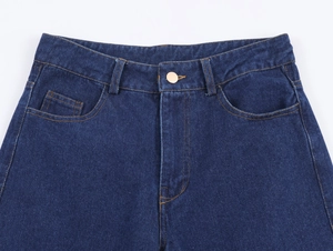 Détail du jean en denim bleu foncé avec coutures contrastées et bouton en métal doré
