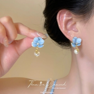 Close-up of model wearing light blue petal earrings with crystal accents and white pearl