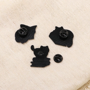 Black enamel cat pins with metal backing and butterfly clutch on beige linen fabric