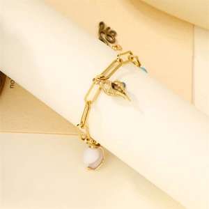 Detailed view of gold shell and conch pendants on a paperclip chain bracelet