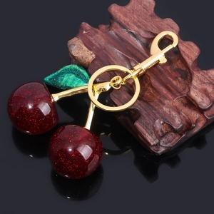 Macro view of cherry keychain with red glitter balls and green leaf on gold lobster clasp
