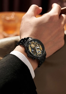 Close-up of skeleton watch dial with gold gears and blue hands on black metal strap