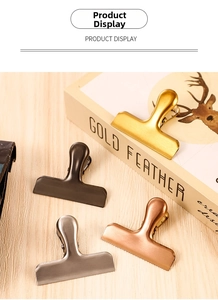 Detail of multi-color stainless steel large binder clips on a wooden tabletop with a book