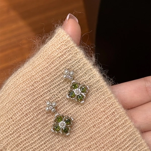 Detail of flower earrings with green stones and pearls on beige knit fabric background