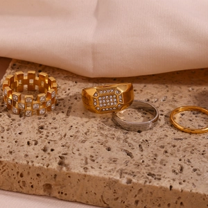 Close-up of four 18K gold and silver rings with pave zircon on a beige stone slab