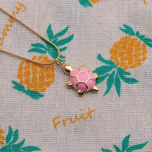 Close-up of a turtle pendant necklace with pink enamel shell and gold plated finish