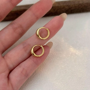 Close-up of small gold huggie hoop earrings held by hand showing polished mirror finish