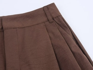 Detail of dark brown pleated pants waistline showing fabric texture and belt loops