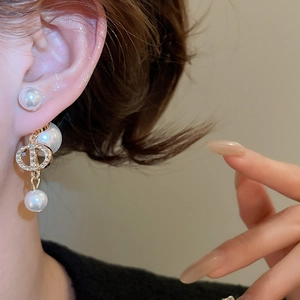 Close-up of gold plated pearl earrings with zircon logo on a female model's ear