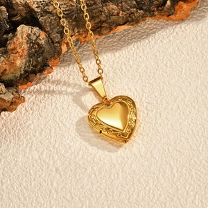 Close-up of a gold heart locket pendant with vintage floral engraving on tree bark