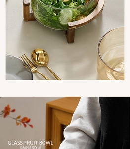 Close-up of clear glass salad bowl with solid wooden stand and golden cutlery on table