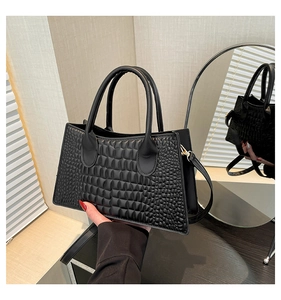 Detail of black handbag showing embossed crocodile texture and dual handle design