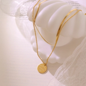 Double layer gold necklace with engraved disc pendant on an elegant shell background