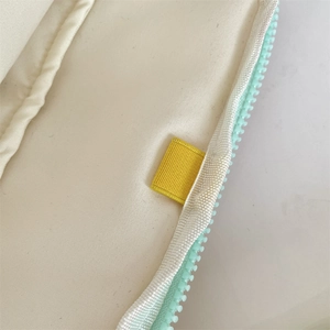 Detalle de funda para portátil en lona crema con cremallera verde menta y marca amarilla