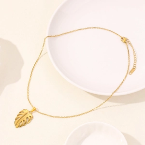 Macro detail of gold ginkgo leaf pendant on elegant chain over ceramic surface