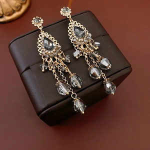 Close-up of golden teardrop tassel earrings with dark grey crystals on leather texture