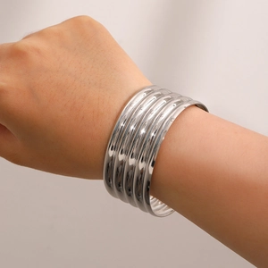 Macro detail of six stacked polished silver stainless steel bracelets worn on wrist