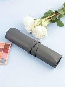 Dark grey leather roll-up makeup brush pouch with strap tie closure on blue background
