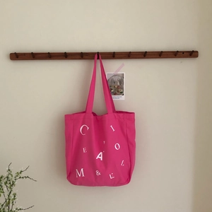 Detailansicht der rosa Canvas-Einkaufstasche mit Buchstabendruck am Holzhaken
