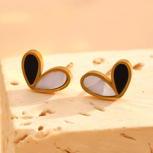 Detail of asymmetrical black and white heart stud earrings on a textured stone surface