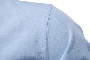 Vue détaillée du tissu en lin bleu clair et des surpiqûres sur l'épaule d'une chemise homme
