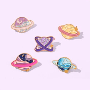 Detail of five colorful enamel planet brooches with starry sky and moon patterns on a purple background