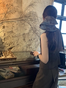 Detail view of a bohemian tie-dye bucket hat and brown pinstripe vest set on a model