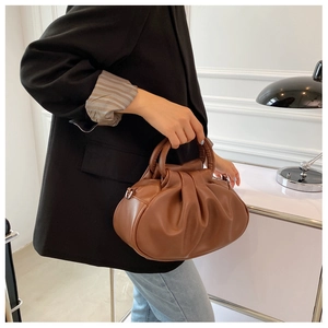 Brown pleated cloud bag being held by a model wearing a black blazer and jeans