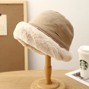 Plush camel winter bucket hat with faux fur trim and metal badge on a wooden stand