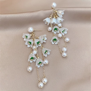 Détail des boucles d'oreilles muguet avec perles blanches sur fond de soie douce