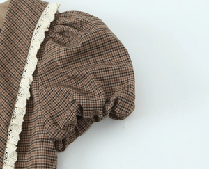 Close-up of brown plaid fabric texture and delicate cream lace trim on a retro dress