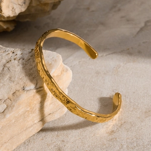 Minimalist gold wave pattern open bangle with hammered texture on natural stone