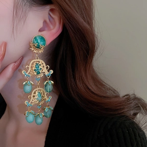 Détail rapproché de boucles d'oreilles dorées ajourées de style rétro avec résine verte