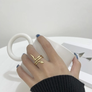 Close-up of a vintage golden snake ring worn on the finger while holding a white mug