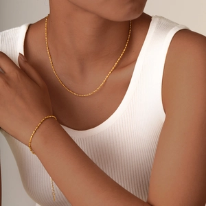 Close-up of minimalist gold beaded necklace and bracelet set on model wearing white top