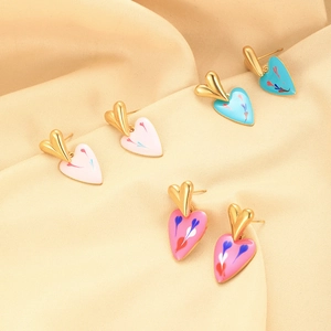 Detailed macro view of colorful enamel heart earrings on soft beige satin fabric