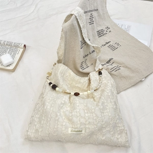 Détail du sac cabas en dentelle blanche avec poignée perlée et étiquette de marque