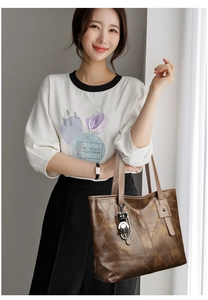 Detail of brown leather tote bag with a gold bear pendant held by a model in a white tee