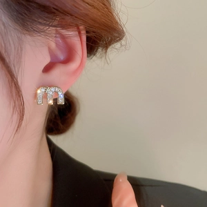Close-up of gold M-letter earrings with pavé zircons worn on model's ear lobe
