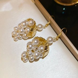 Macro shot of gold shell accents and glossy white pearl grape cluster dangle earrings