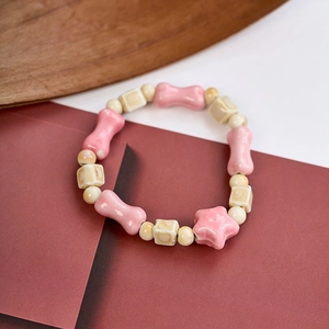 Close-up of a handmade ceramic bracelet featuring pink bow and star beads on wood background