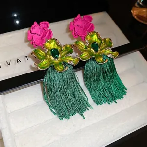 Boucles d'oreilles bohèmes avec fleurs en émail vert et longs pompons dans un écrin