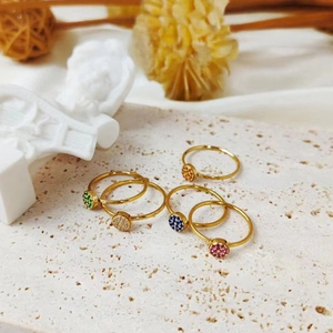 Set of five gold plated rings with colorful round cubic zirconia on a white stone slab